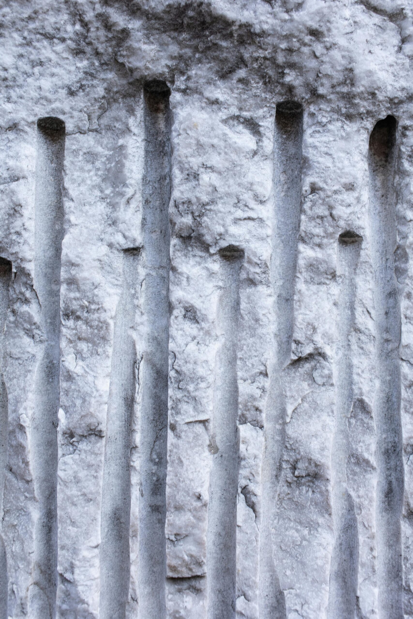 Detailed image of a textured concrete wall featuring distinct vertical grooves, ideal for background use.